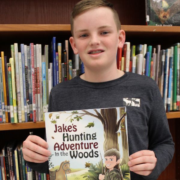  sixth grade boy holding a book with library shelves behind him